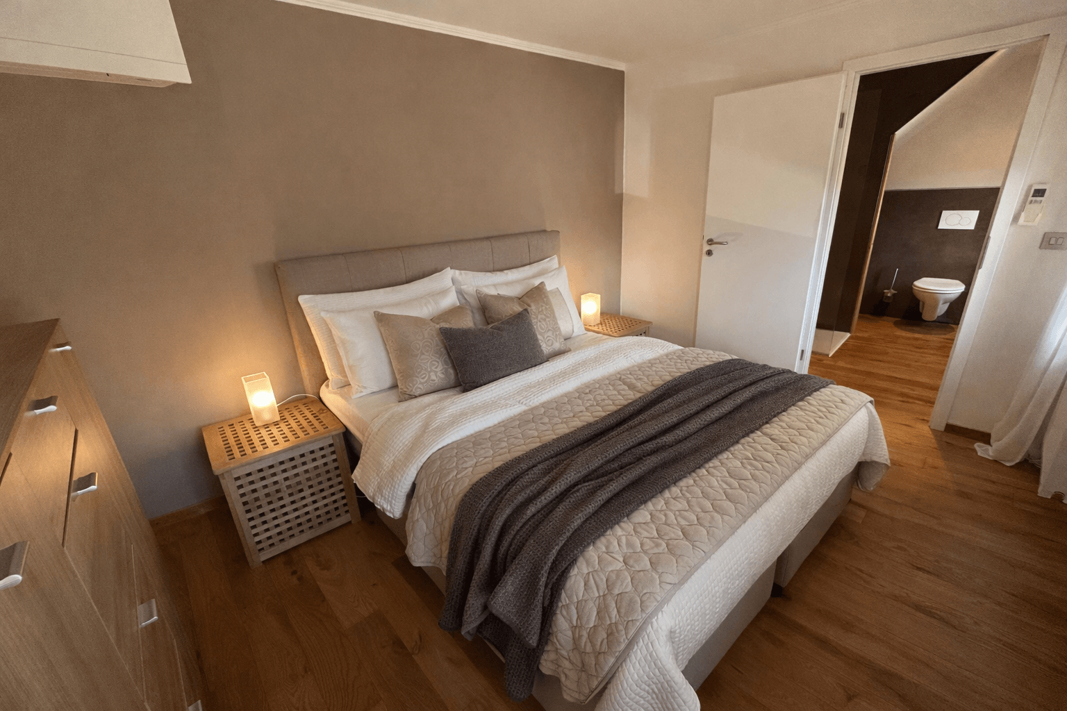 Schlafzimmer mit Ansicht des Ehebettes mit vielen Kissen in warmer Atmosphäre